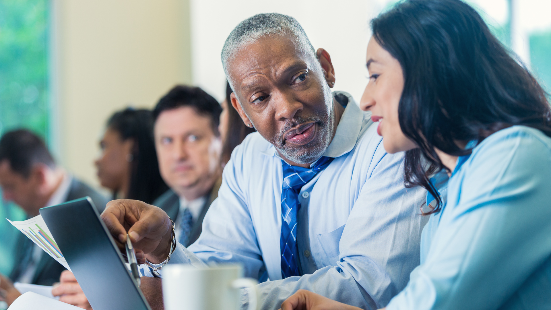 Senior African American businessman talks with mid adult Hispanic female businesswoman at a professional seminar.