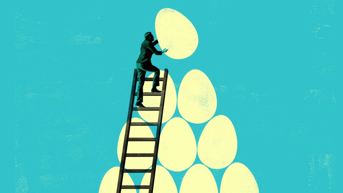 a silhouette of a person on top of a ladder stacks one final large white egg on a pile of large white eggs against a blue background